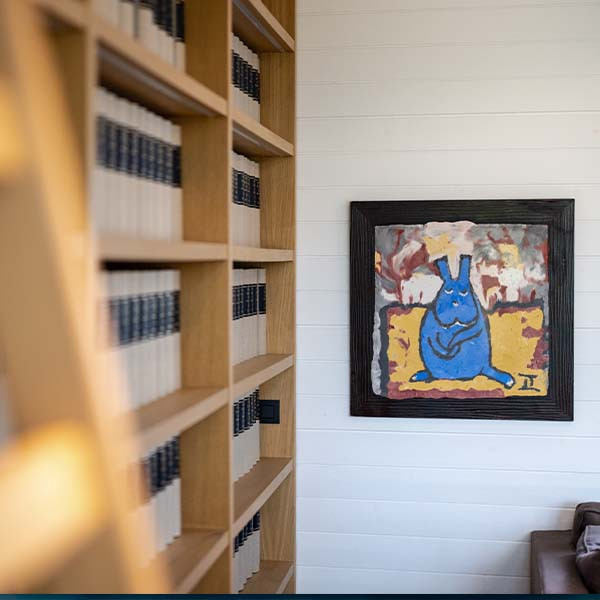 Photo d'une salle avec etagere à livres avec un tableau representant un lapin bleu.